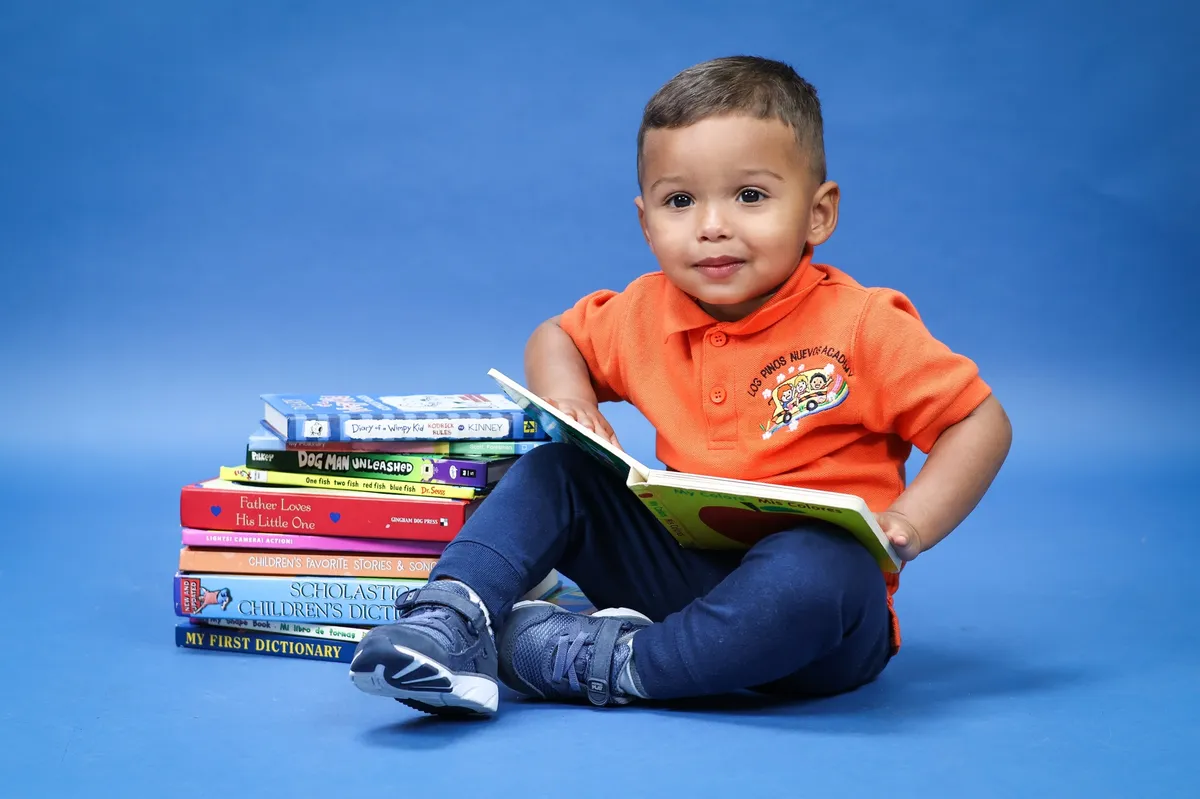 Niño de dos años con uniforme naranja leyendo un libro ilustrado sentado en el piso